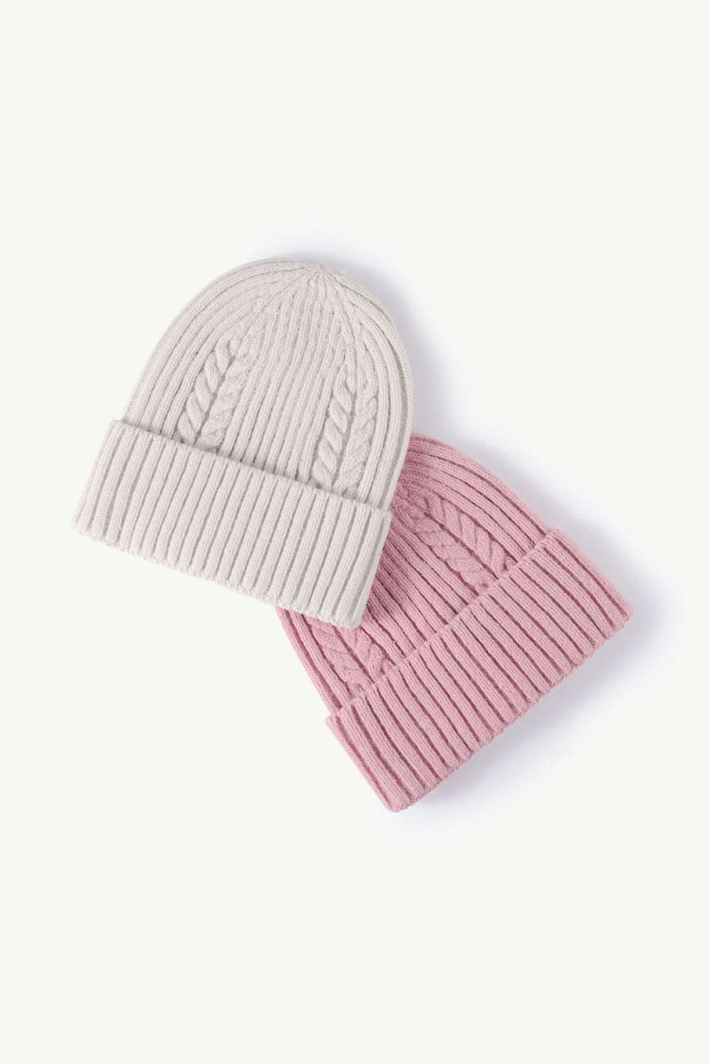 White and pink Cable-Knit Cuff Beanies displayed together, showcasing a stylish color combination with textured knit patterns and fold-over cuffs for a cozy, fashionable winter look.